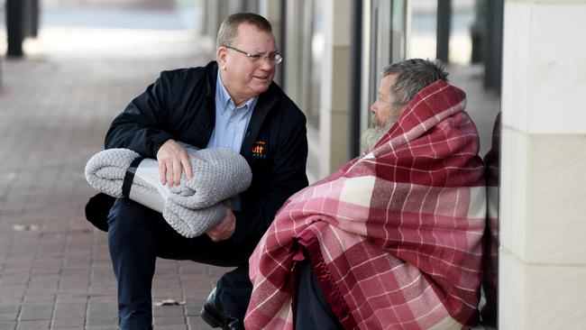 Hutt St Centre chief executive Chris Burn, pictured giving a homeless man a blanket, says the review is a waste of money. Picture Mark Brake