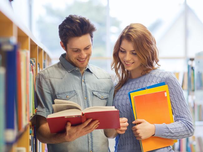 people, knowledge, education and school concept - happy student couple with books in library