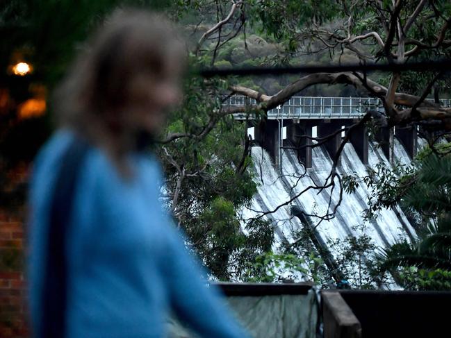 A woman walks in front of the overflowing Manly Dam on Tuesday soon after an evacuation order was issued for residents living below the dam. The order was later withdrawn. Picture: Muhammad FAROOQ / AFP)