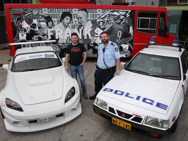 Senior Constable Steven Planinic stands near a Police car from the 80s, alongside Frank's Cheesesteak and Dogs owner Antonio Tarzia. Photo: Robert Pozo