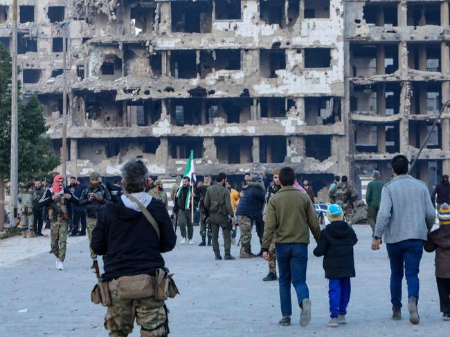 Syrian rebel fighters and civilians gather in the heart of the central city of Homs early on December 8, 2024, after rebel forces entered Syria's third city overnight. Hayat Tahrir al-Sham (HTS) and allied anti-goovernment factions have pressed a lightning offensive since November 27, sweeping swathes of the country from government control, including major cities Aleppo, Hama and Homs. (Photo by Bakr ALKASEM / AFP)