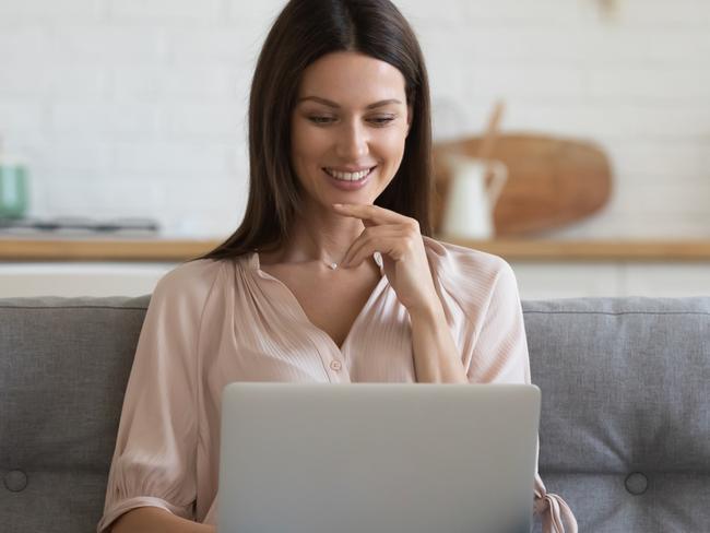 Smiling young woman using laptop, sitting on couch at home, beautiful girl shopping or chatting online in social network, having fun, watching movie, freelancer working on computer project