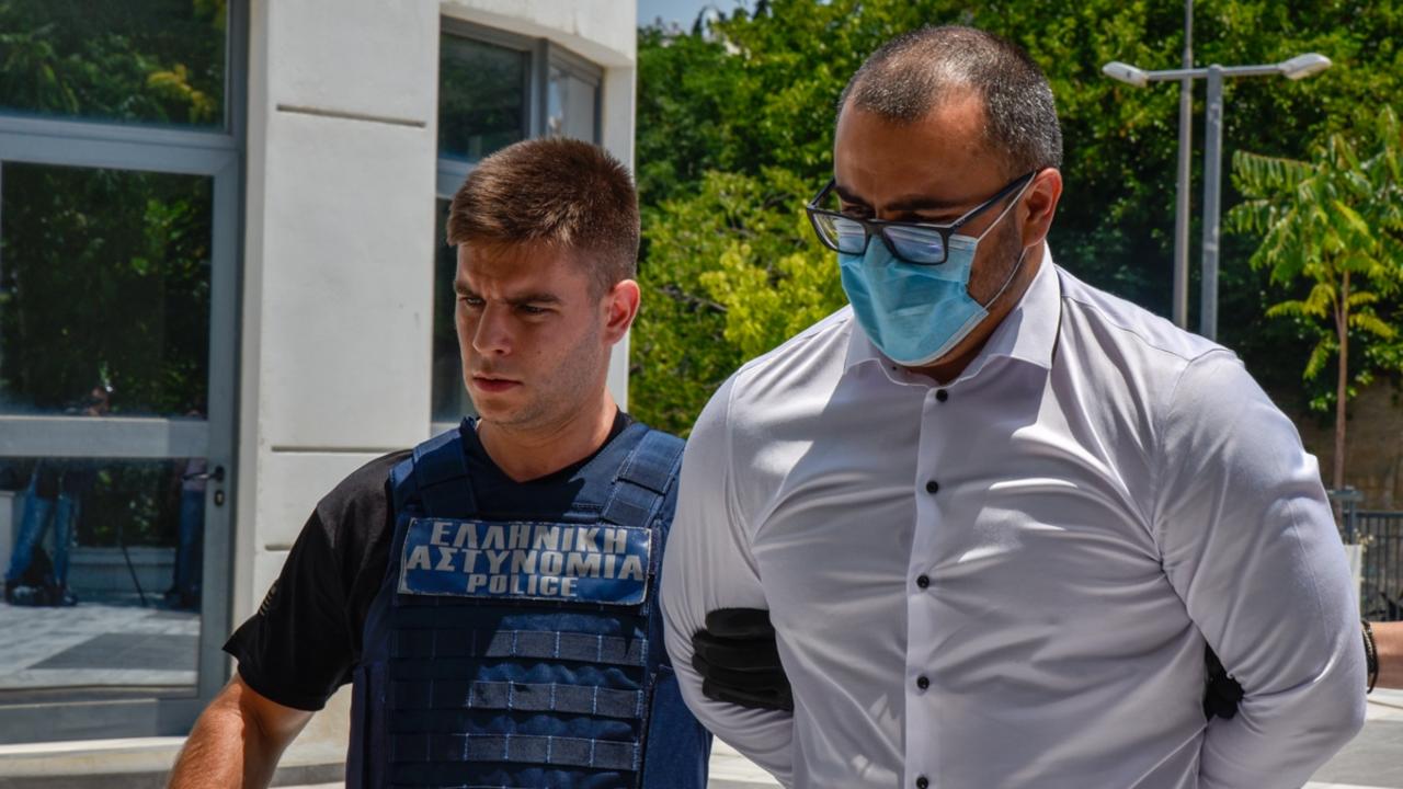 Milen Raychev, the brother of Yuliyanov J Raychev Serafim, who is accused of being an accessory to the murder of John Macris, is lead into court in Athens by two police officers. Picture: Spyros Bakalis