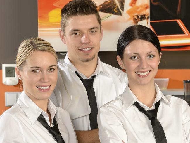 Three smiling server posing in uniform in cafe