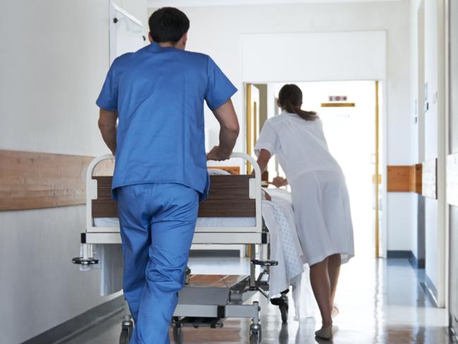 Rearview shot of hospital staff wheeling a patient in a gurney down a corridor