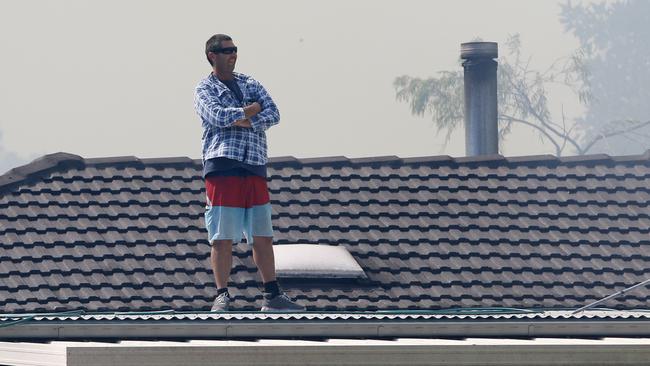 A man stands on the roof of his house as a bushfire approaches, on Lemon Tree Passage Rd in Salt Ash, on Friday morning. Picture: AAP