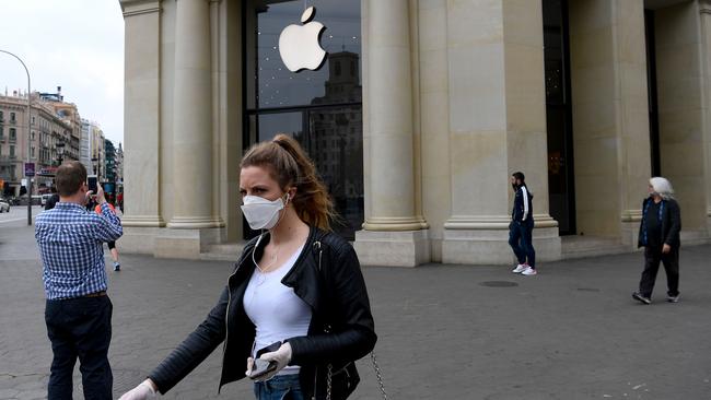 A woman wearing a face mask walks past the closed Apple store in Barcelona on March 14, 2020 after regional authorities ordered all shops in the region be shuttered from today through March 26, save for those selling food, chemists and petrol stations, in order to slow the coronavirus spread. (Photo by Josep LAGO / AFP)