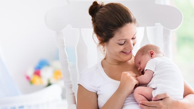 Young mother holding her newborn child. Mom nursing baby. Woman and new born boy relax in a white bedroom with rocking chair and blue crib. Nursery interior. Mother breast feeding baby. Family at home