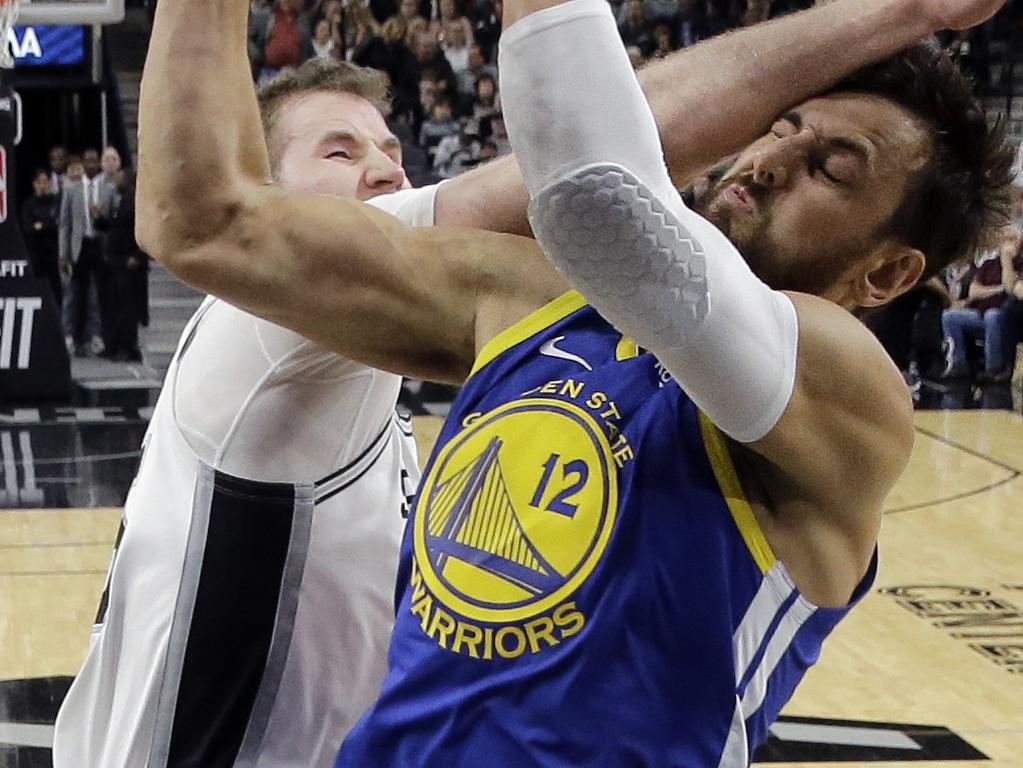 Golden State Warriors center Andrew Bogut (12) is hit across the face as he scores against San Antonio Spurs center Jakob Poeltl (25) during the first half of an NBA basketball game, in San Antonio, Monday, March 18, 2019. (AP Photo/Eric Gay)