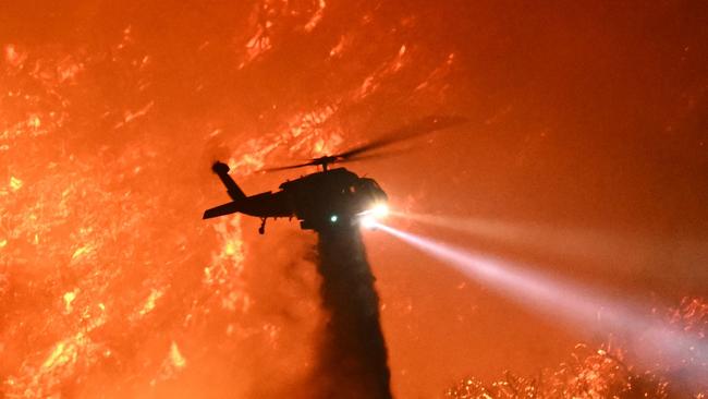 A fire fighting helicopter drops water as the Palisades fire grows near the Mandeville Canyon neighborhood and Encino, California, on January 11, 2025. The Palisades Fire, the largest of the Los Angeles fires, spread toward previously untouched neighborhoods January 11, forcing new evacuations and dimming hopes that the disaster was coming under control. Across the city, at least 16 people have died as multiple fires have ripped through residential areas since January 7, razing thousands of homes in destruction that US President Joe Biden likened to a "war scene." (Photo by Patrick T. Fallon / AFP)