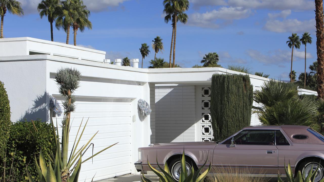 White Mid Century architecture home with vintage Mauve Lincoln Continental Mark V parked in the driveway.