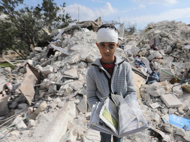 A Syrian boy, who lost his family and was also wounded carries a book as he stands amid the rubble of his family home in the town of Jindayris, in Syria's Aleppo province. Picture: AFP