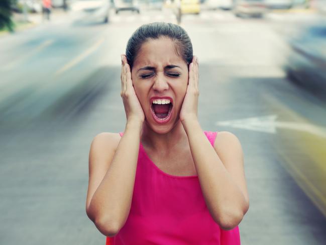 Portrait of woman standing still in the middle of a street with cars passing by fast, screaming stressed and frustrated