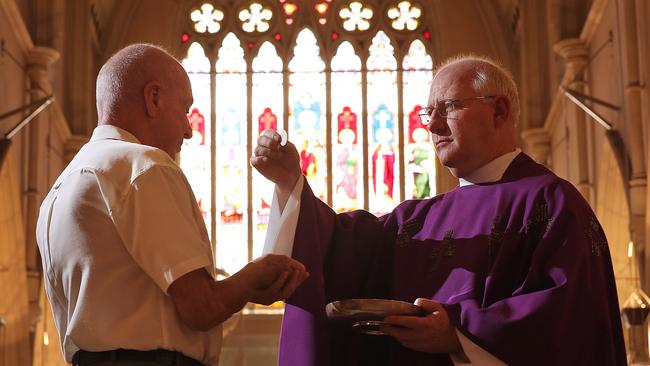 Dean of Brisbane’s St Stephen’s Cathedral, Father Anthony Mellor, administers the sacrament to long-time parishioner Maurie Brewer. Picture: Lyndon Mechielsen