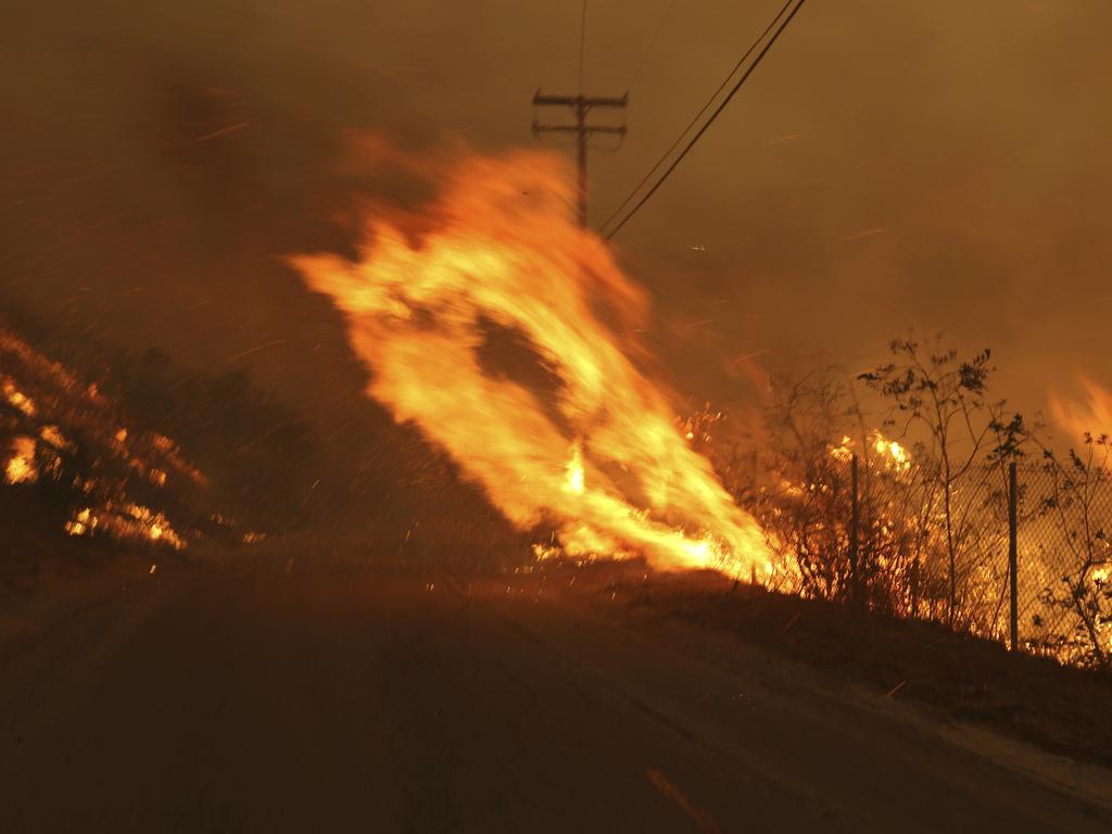 Wind-driven flames from a wildfire race up a slope and cross the road in Malibu. Picture: AP