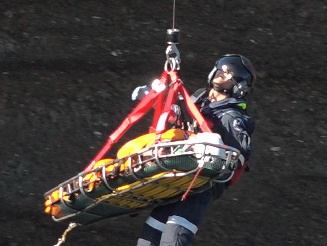 The rescued cliff jumper as he is being winched to the Westpac rescue helicopter. Picture: David Cleverly