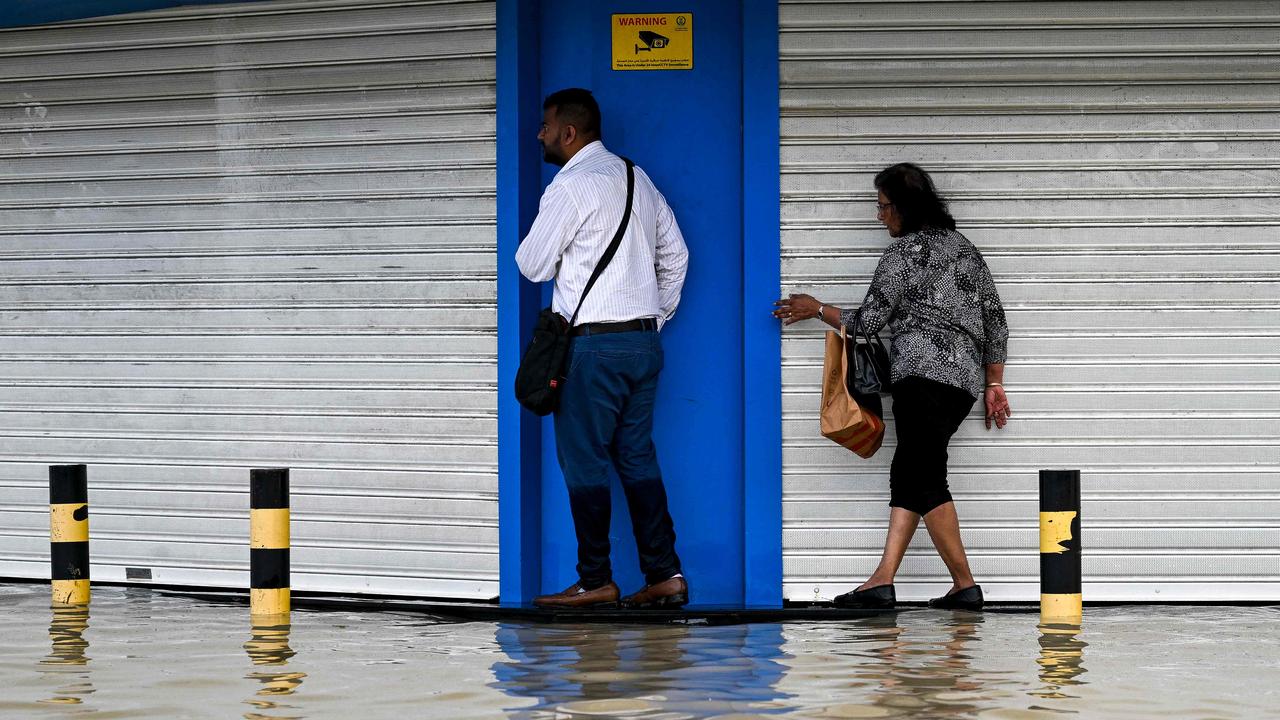 People try to avoid getting wet as they cross a flooded street. Picture: Ahmed RAMAZAN / AFP