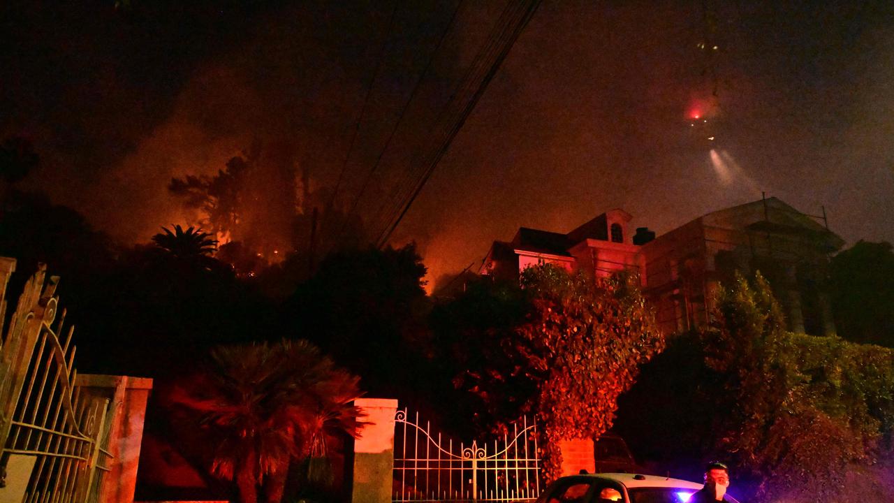 A police officer stands below burning brush at the Sunset Fire near Hollywood Blvd in the Hollywood Hills. (Photo by Robyn Beck / AFP)