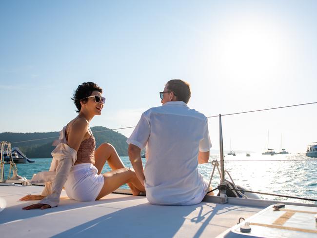 Caucasian couple enjoy outdoor luxury party drinking champagne with talking together while catamaran boat sailing at sunset. Man and woman relax with outdoor lifestyle sail yacht on summer travel vacation; rich couple wealth generic