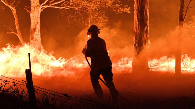 A firefighter desperately hoses down trees and flying embers in an effort to secure nearby houses from bushfires near Nowra on New Year's Eve. Picture: Saeed Khan/AFP