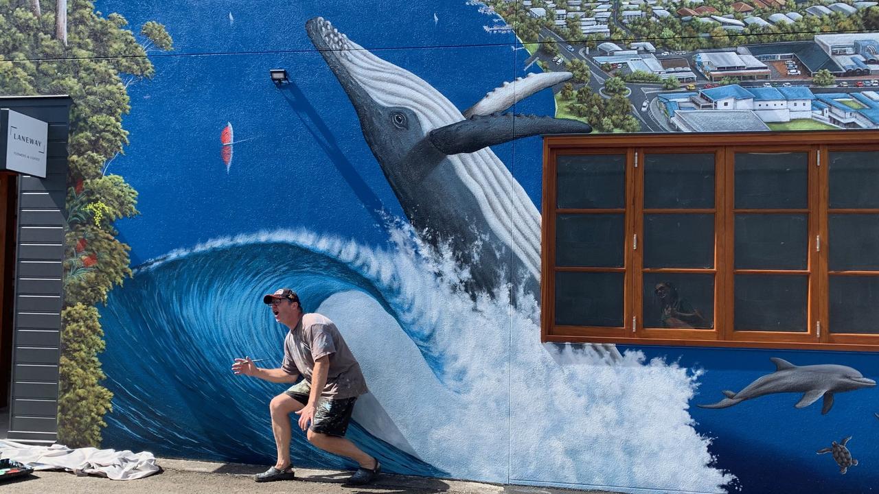 Artist Andrew Grassi tucks into a barrel he painted onto a wall in Thomas St in Noosaville.