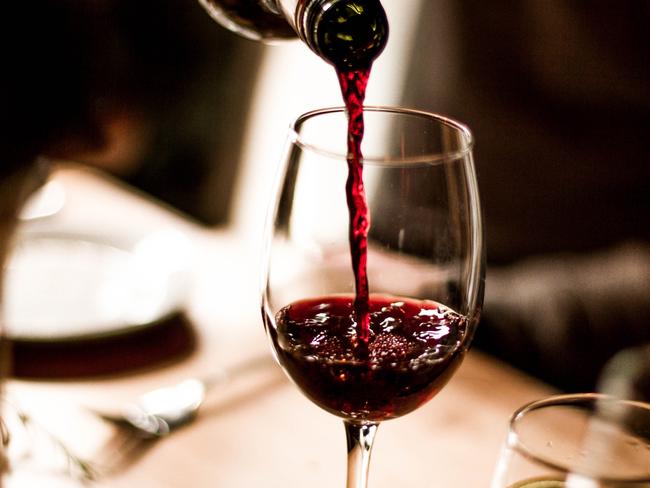 Red wine being poured into a stem glass at the table.