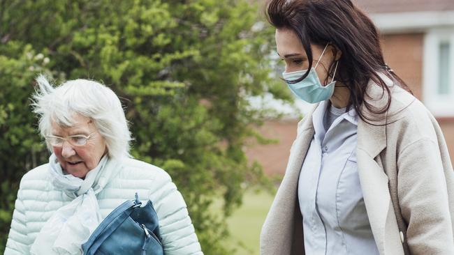 A side view of a female healthcare worker wearing a protective mask walking her grandmother home during the Coronavirus pandemic.