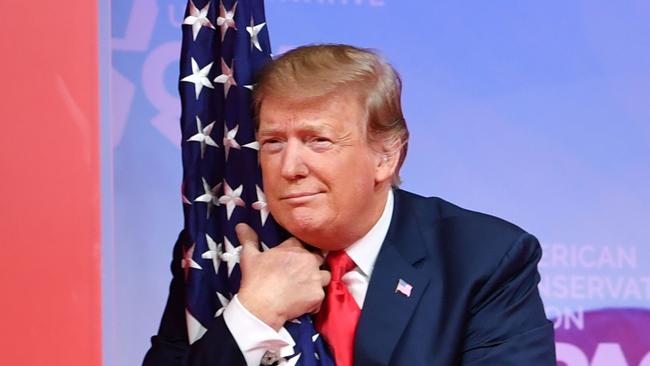 TOPSHOT - US President Donald Trump hugs the US flag as he arrives to speak at the annual Conservative Political Action Conference (CPAC) in National Harbor, Maryland, on March 2, 2019. (Photo by NICHOLAS KAMM / AFP) / ALTERNATIVE CROP