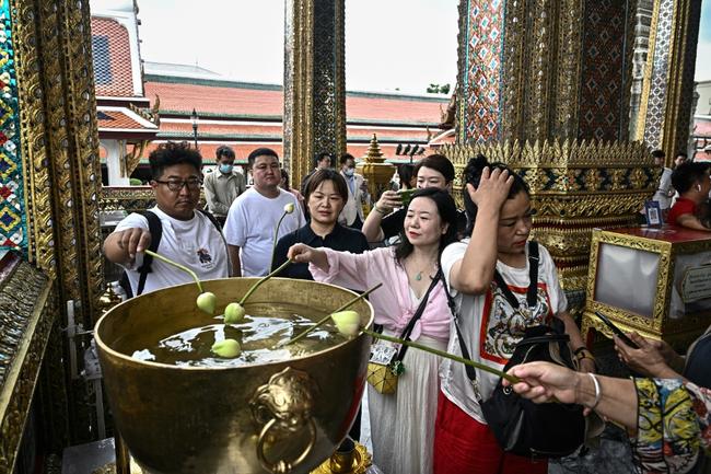 Chinese tourists dipping lotus bulbs in a water bowl, at the Grand Palace in Bangkok