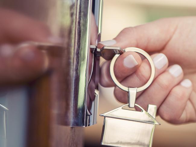 Woman using a house key on the front door. Close up of he woman??s hand. She is turning the key in the lock. There is a hallway in the  background. The key ring has a house icon on it.