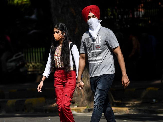 A woman wearing a facemask and a man wearing a scarf over the face as a preventive measure against the spread of Covid-19 coronavirus cross a street in New Delhi on September 12, 2020. (Photo by Sajjad  HUSSAIN / AFP)