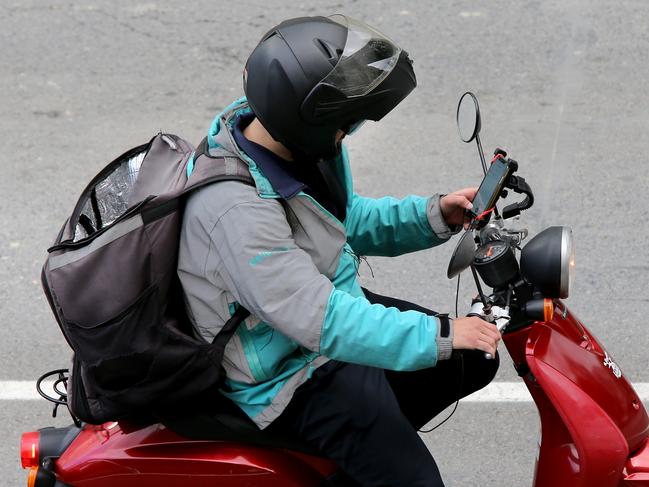 A food delivery driver uses his mobile phone while riding. Picture: AAP/David Clark