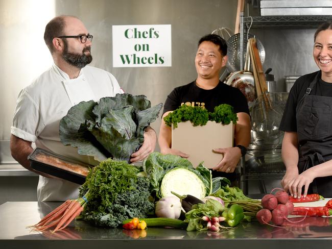 27.3.2020 - Chefs Paul Baker from Chefs on Wheels with Terry Intarakhamhaeng, head chef Soi 38 and Emma McCaskill, head chef at Sparkke at the Whitmore, cooking up a storm in the Edible Exchange kitchen in Glynde; Chefs on Wheels is a unique initiative that has Adelaide's top chefs cooking ready made meals, deliveries done by local company edible exchange. They're using producers who are no longer getting orders from restaurants, so it saves a lot of jobs all-round. Photo - Naomi Jellicoe