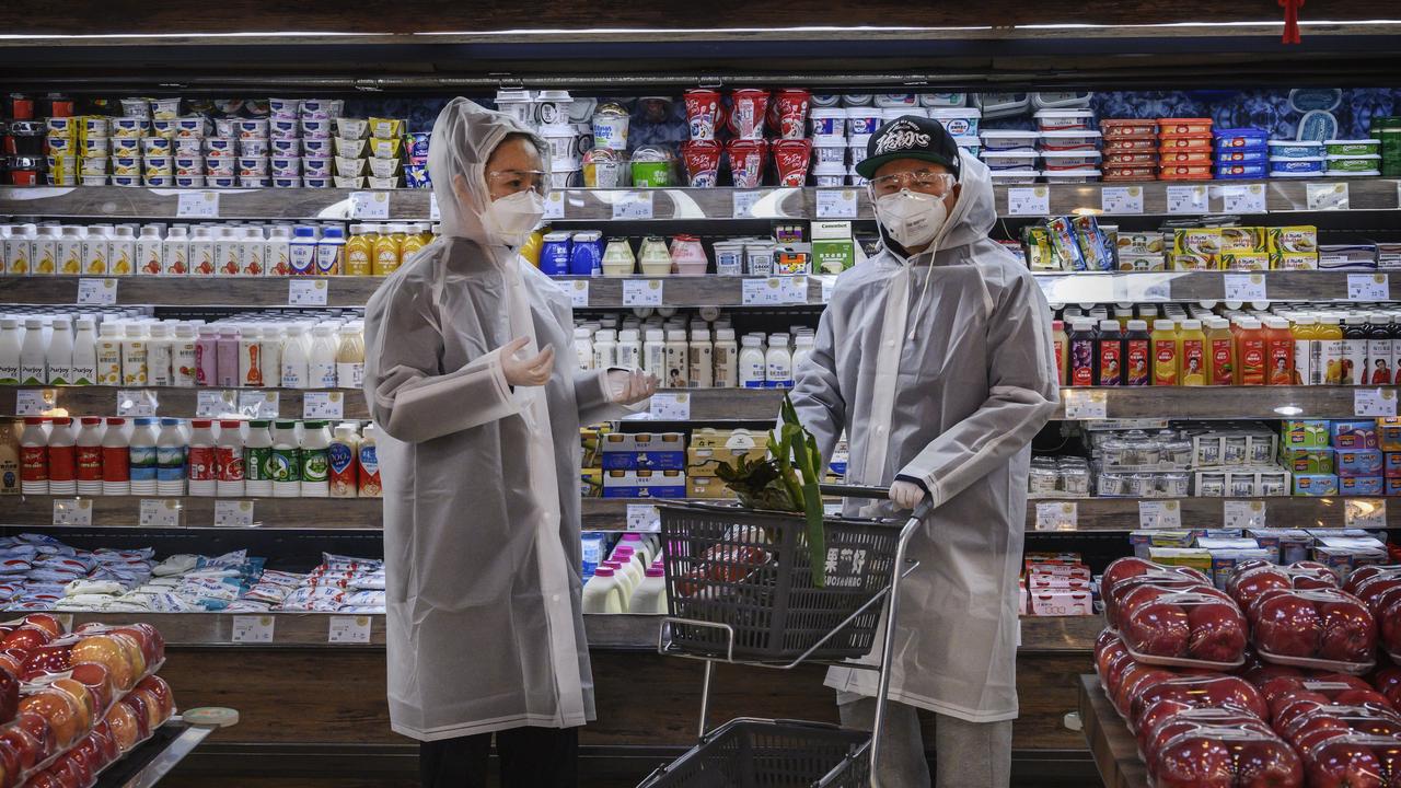 A Chinese couple wear plastic coats and masks while they go grocery shopping in China. Picture: Kevin Frayer/Getty Images