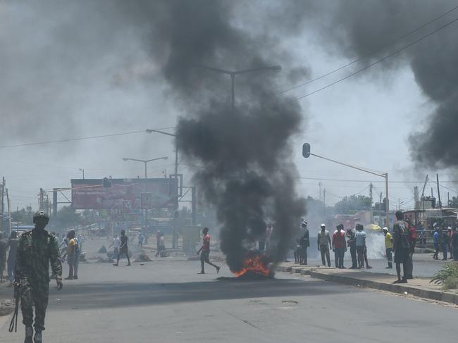 TOPSHOT - A Mozambican soldier walks away as protesters burn tyres during a demonstration against the government in Maputo on December 6, 2024. According to the civil society platform 'Plataforma Decide' (Decide Platform) at least 90 people have been killed during the ongoing clashes between protesters and security forces since protest started on October 21, 2024, a few days after two oppositions figures were killed following the Mozambican election on October 9, 2024. (Photo by Amilton Neves / AFP)