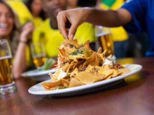 Close up on nachos at a sports bar while friends are watching a game