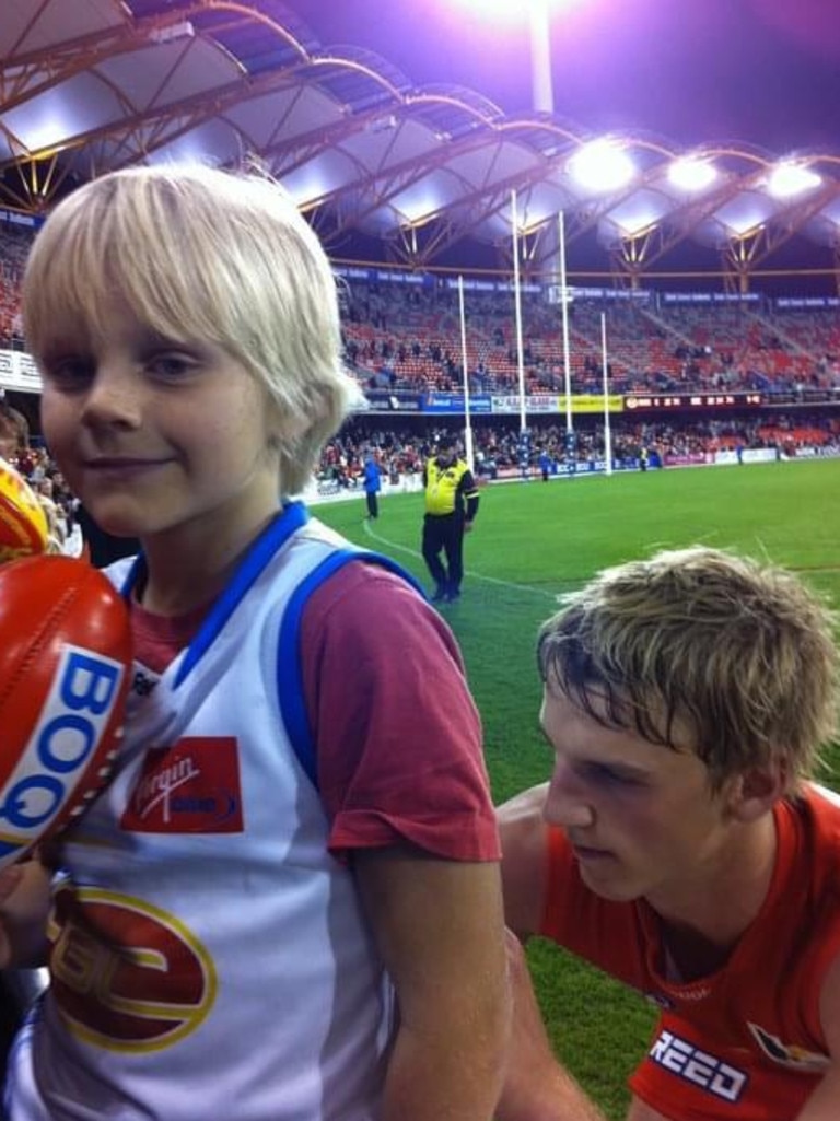 Current Gold Coast Suns player Bodhi Uwland as a child (left) gets his jumper signed by former Suns player Trent McKenize.