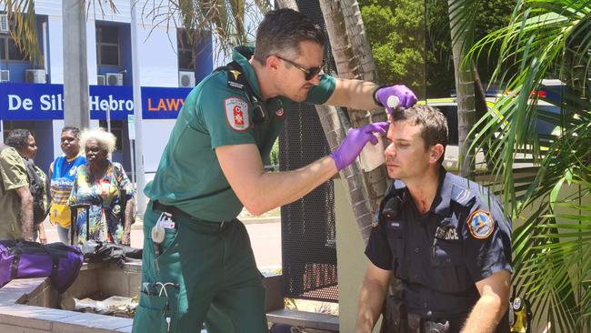 A police officer is helped by a paramedic after he was hit by a glass bottle, allegedly thrown by a man police are trying to apprehend in a police incident on Wood St, Darwin. Picture: Thomas Morgan