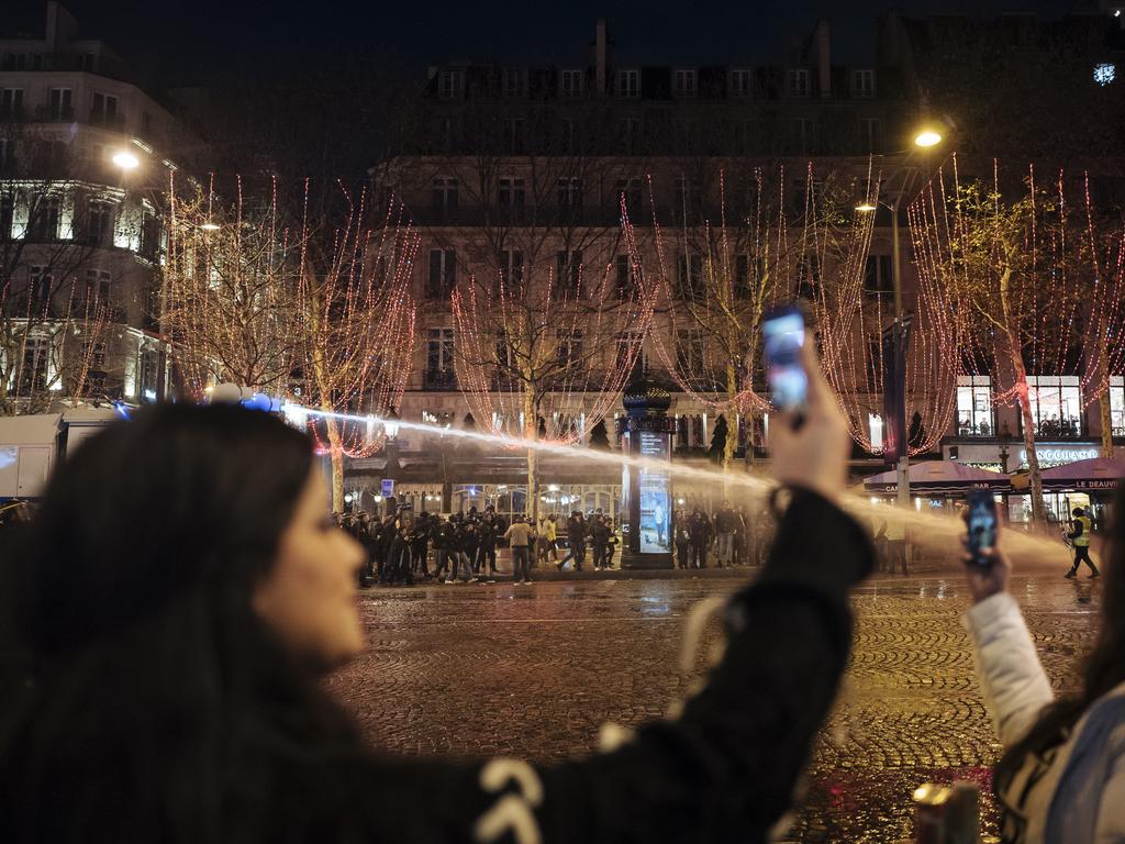 A police water canon operates on the Champs Elysees avenue as tourists in the foreground take pictures of the demonstration in Paris. Picture: AP