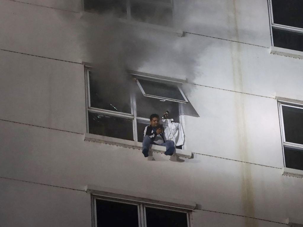 A man sits on a window ledge as a fire burns through the Grand Diamond City hotel-casino in Poipet. Picture: AFP