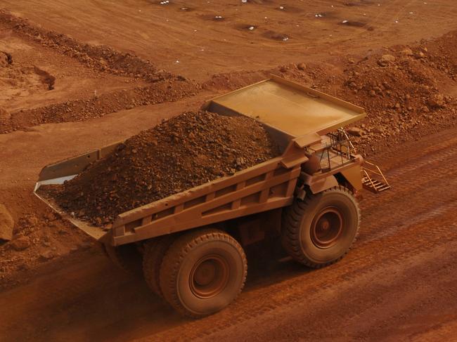 A large haul truck carrying a load of crushed rock and ore on a mine site passing in front of an area being drilled in preparation for blasting; iron ore mining Australia