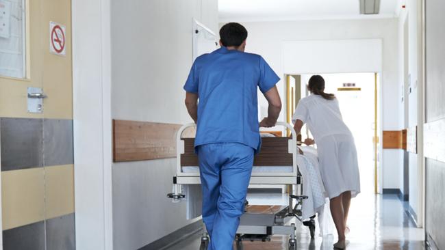 Rearview shot of hospital staff wheeling a patient in a gurney down a corridor