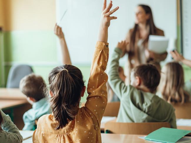 Students raising hands while teacher asking them questions in classroom