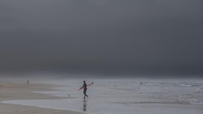 A surfer at Middleton leaves the beach as storm clouds roll in on Sunday, January 7. Picture: Brett Hartwig