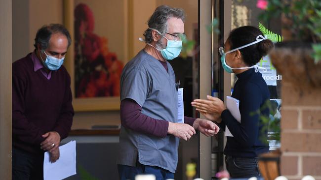 People wearing face masks are seen at the entrance of the Menarock Life aged care facility, where a cluster of some 28 new infections had been reported, in the Melbourne suburb of Essendon.