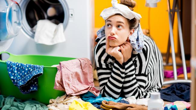 Unhappy housewife sitting with socks near the washing machine with colourful clothes on the floor at home. Picture: iStock