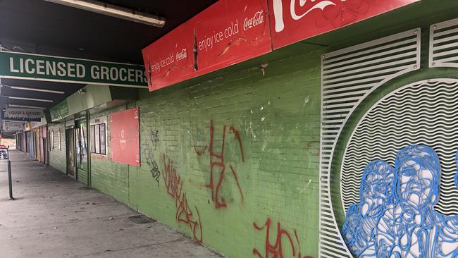 Graffitied shop fronts, mostly closed, on Moresby Court shopping strip.