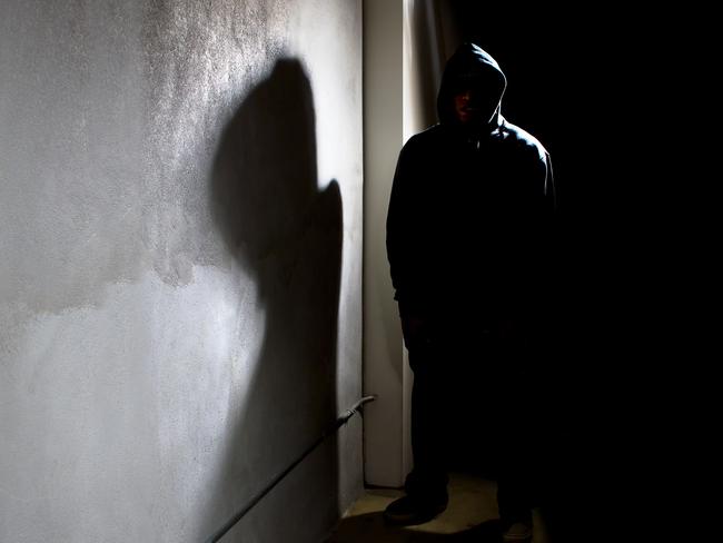 Photo of a hooded criminal stalking in the shadows of a dark street alley.  The hooded man is a silhouette and hiding in the dark.  The man is a criminal waiting to ambush victims.  The concrete walls provide copyspace.The photo depicts crime.  - istock