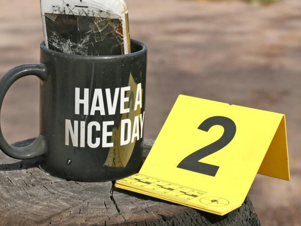 An evidence marker next to a mug labelled with the words “have a nice day” and a smashed iPhone inside.