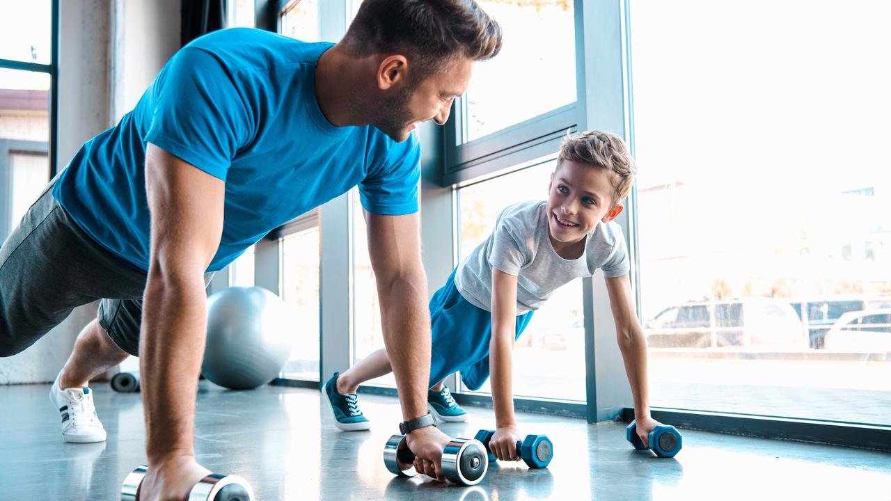 happy father looking at cheerful son and exercising with dumbbells